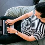 A man in a striped shirt using a laptop on a bean bag, embodying relaxed productivity.
